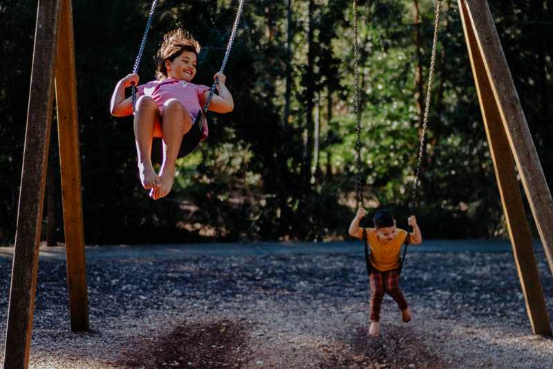 young girl and toddler boy on swings at golden hour