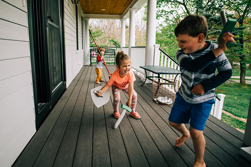 3 children playing with toy swords on house porch