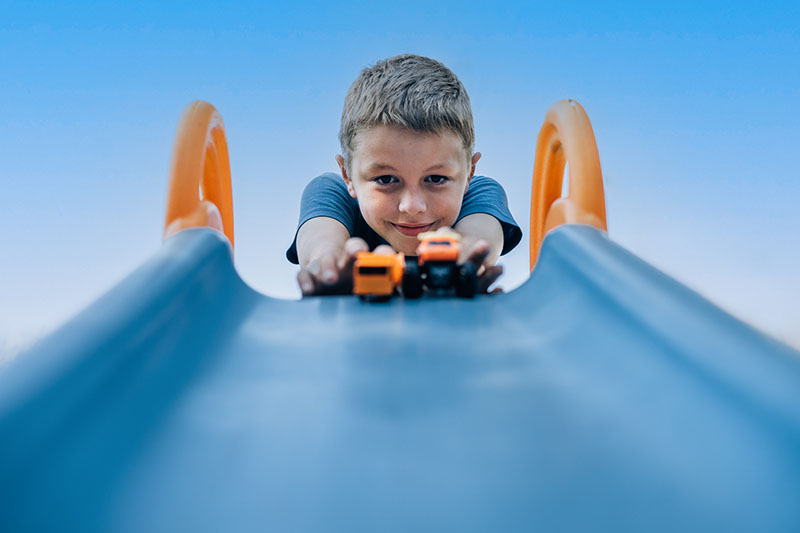 School age boy pushing toy cars down blue slide