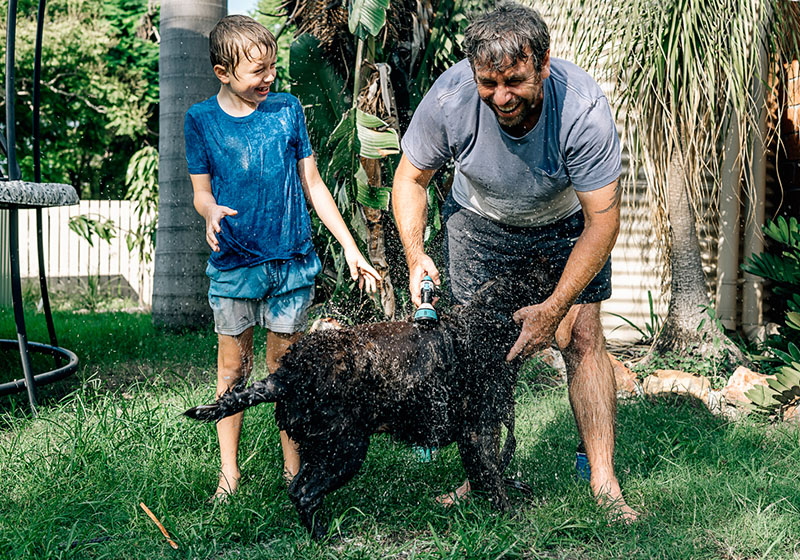 father and son washing black dog