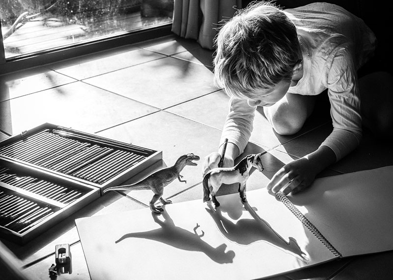 black and white photo of young boy tracing dinosaur shadows