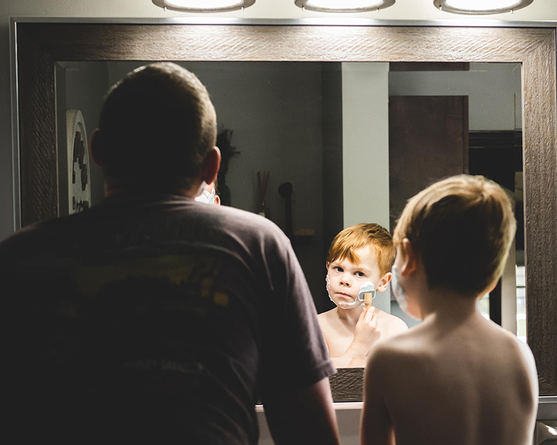 red haired boy shaving with dad in mirror