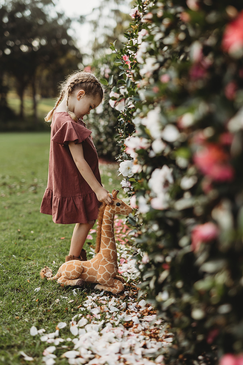 documentary style photo of girl in pink dress with giraffe in garden