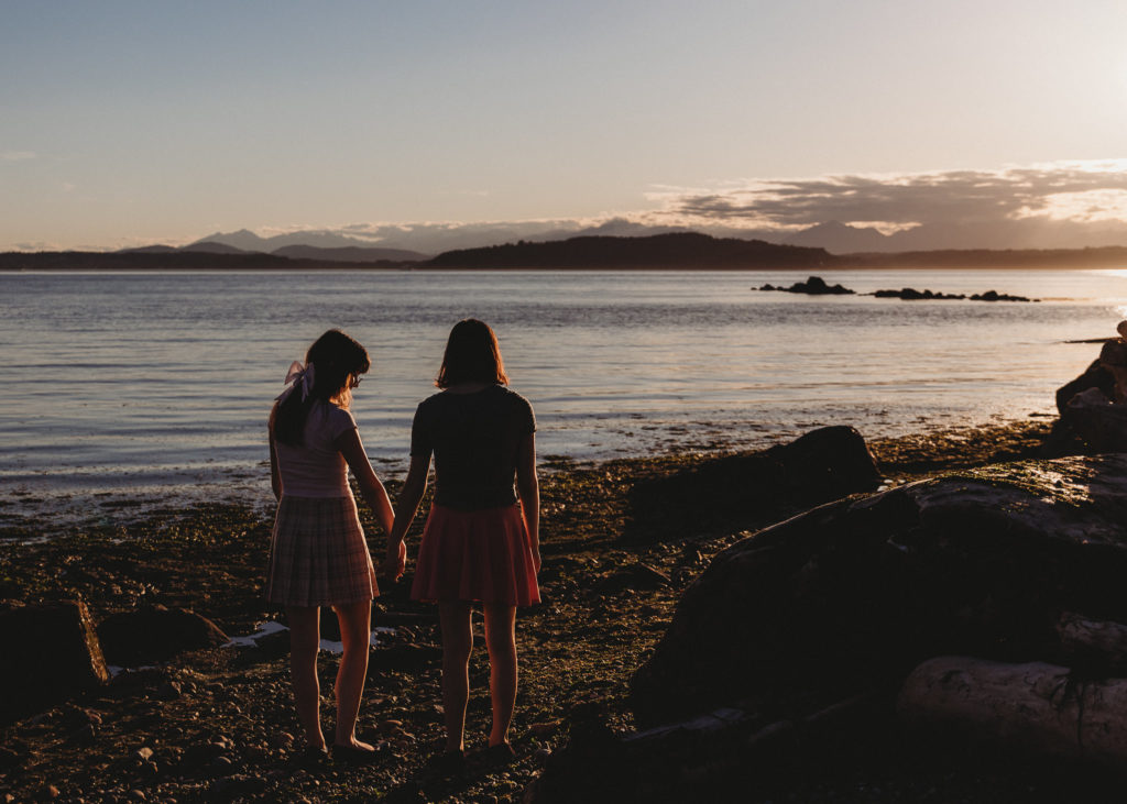 teenage twin sisters holding hands and looking over a lake