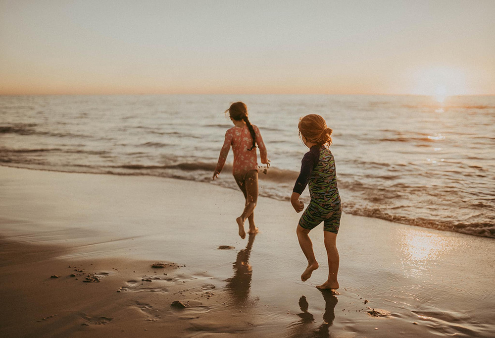two young children running along the beach at golden hour