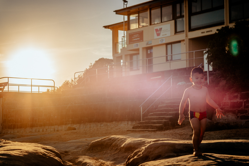 toddler boy walking on beach at golden hour with purple lens haze