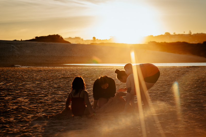 four children backlit building sand castle on the beach with sunflare