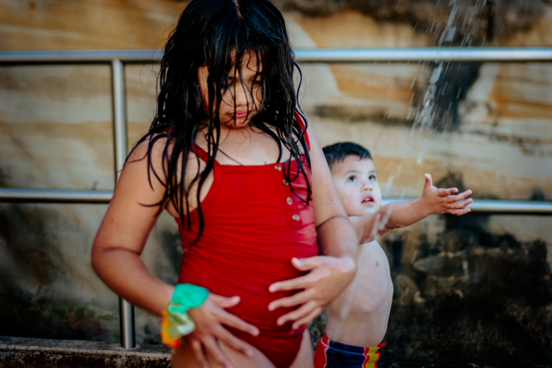 young girl in red swimsuit and toddler boy under beach shower