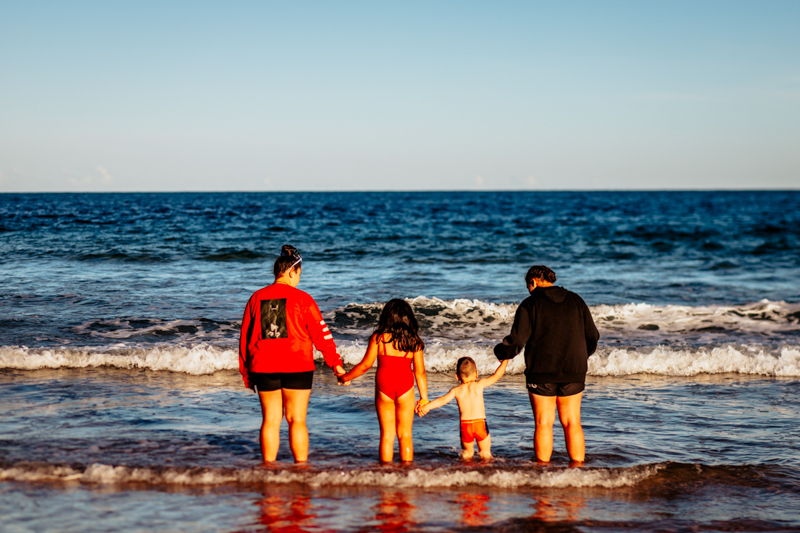faceless portrait of four siblings standing in the ocean staring out to sea