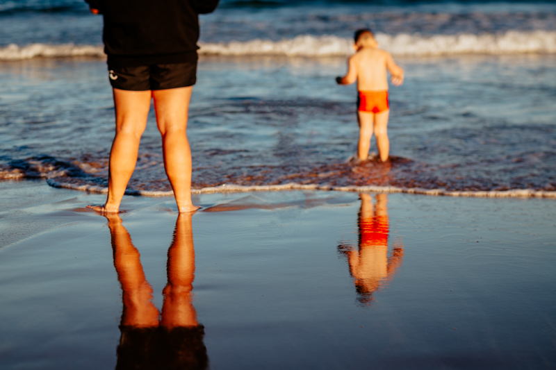 faceless portrait of teenager and toddler standing in the ocean with reflection