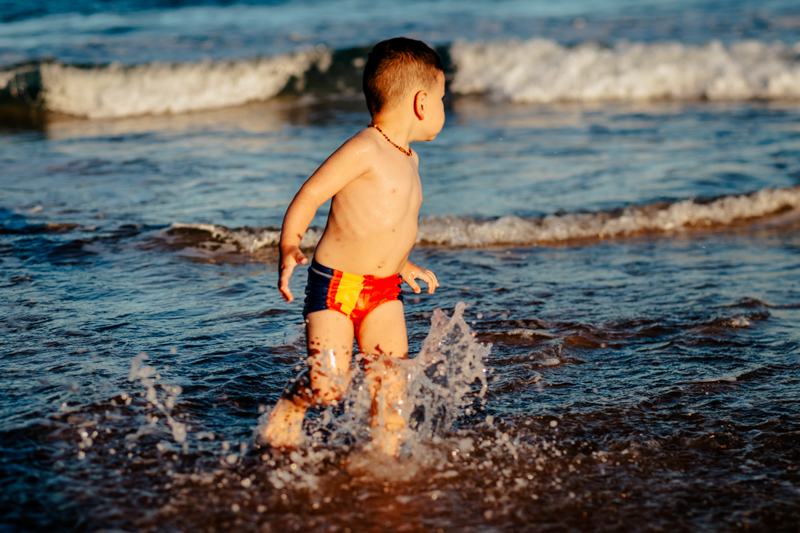 toddler boy in red and blue trunks running in the ocean