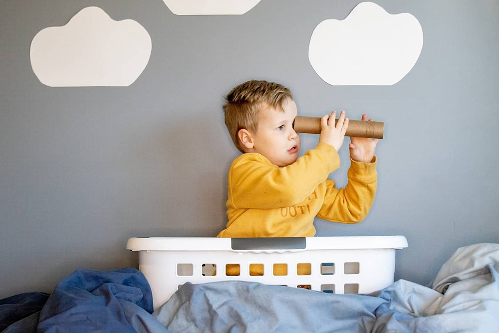 young boy in washing basket boat with cardboard tube telescope