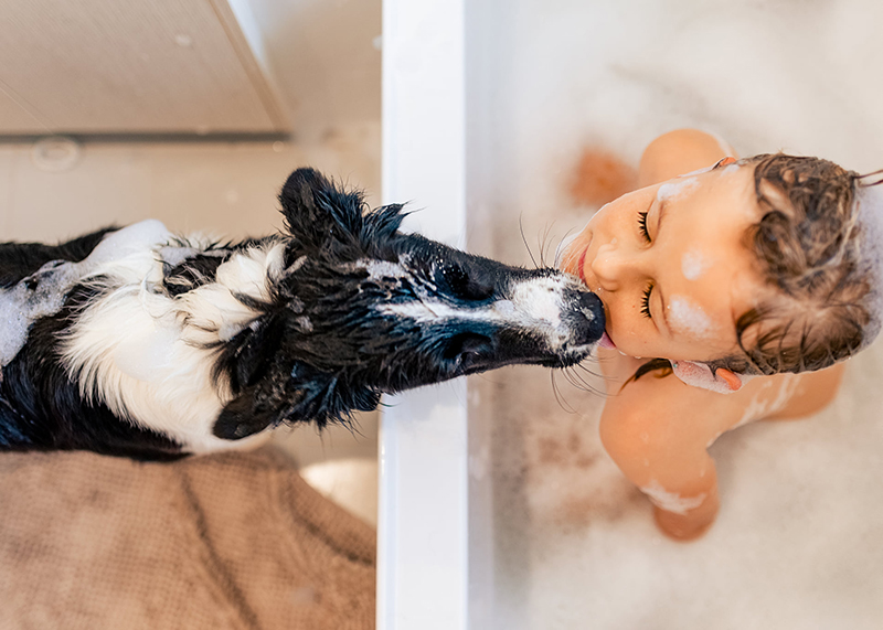 young girl in bath filled with bubbles kissing dog