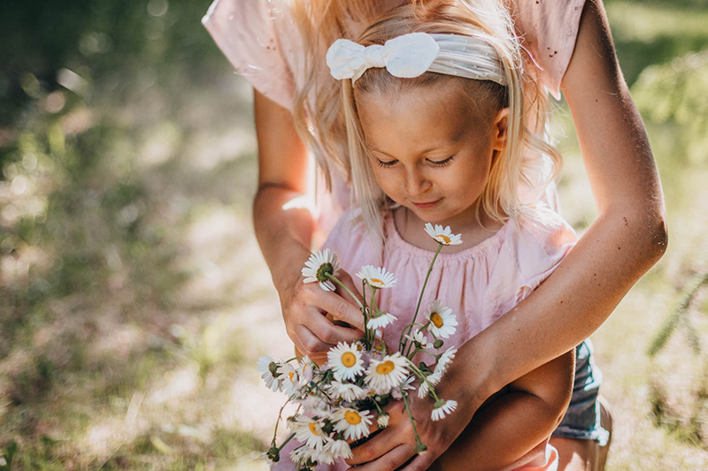 blonde toddler girl holding wildflowers being embraced by older sister