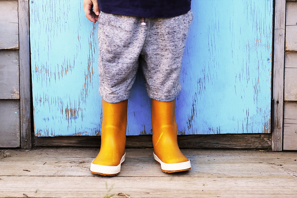 toddler in yellow gumboots against blue door