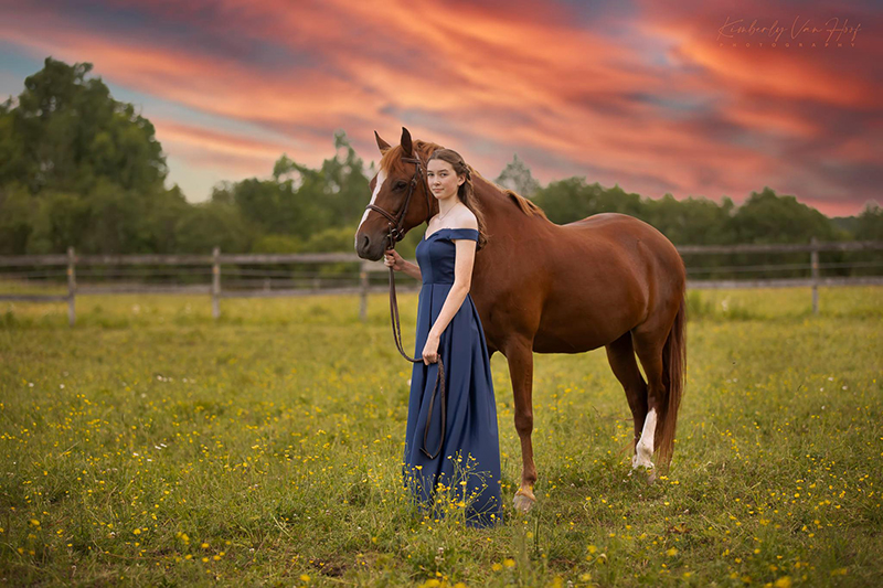 girl in blue dress with a horse in a field