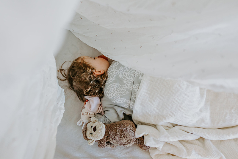 baby sleeping with soft toys and white blankets