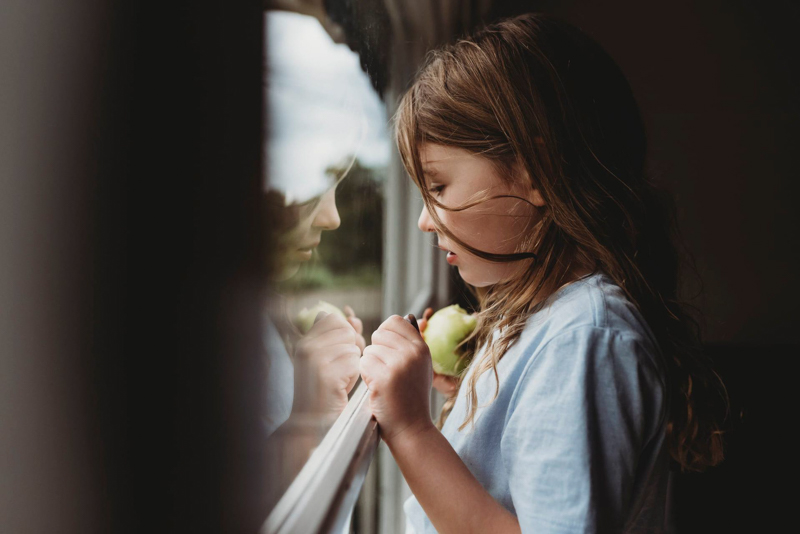 young girl eating apple staring out window