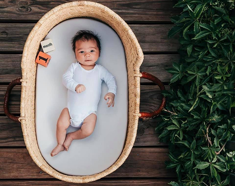 baby in a white romper laying in a basket