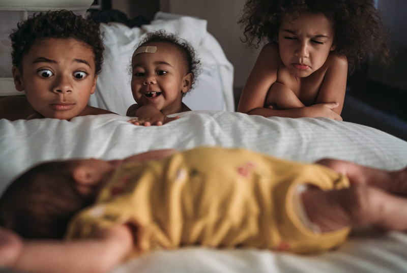 three young siblings watching baby sister sleep