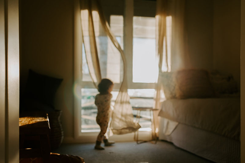 young girl playing in sheer curtain by window light