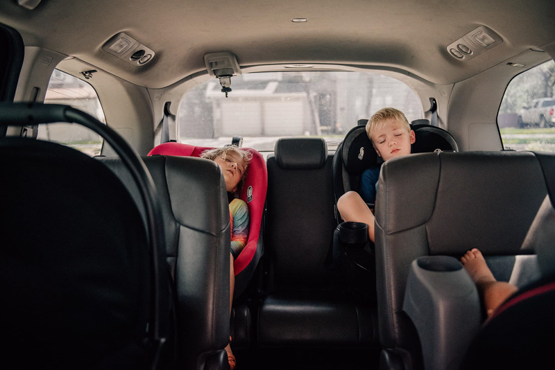 two children asleep in child restraints in the back of the car