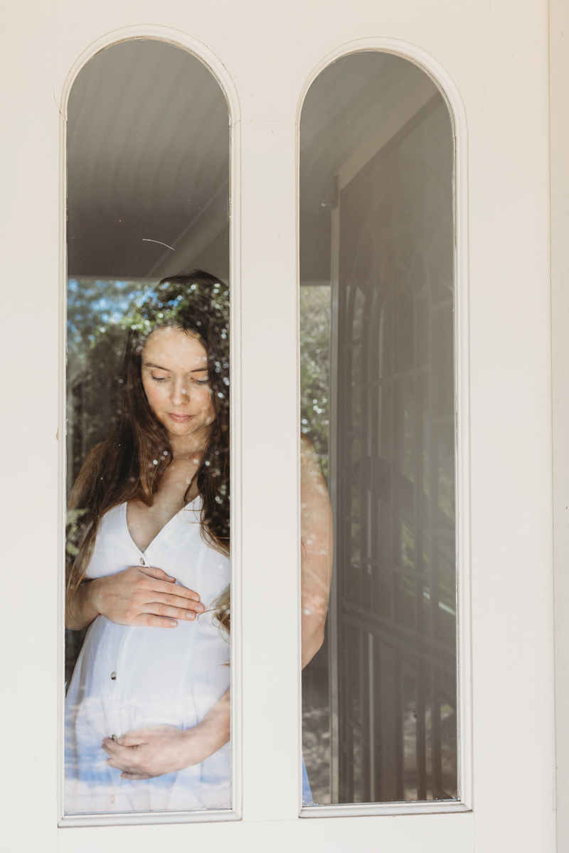 portrait of pregnant lady in white dress inside glass door