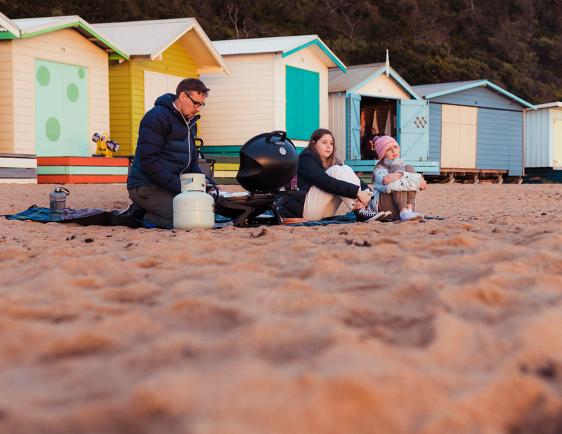 Family sitting on sand in front of colourful beach huts