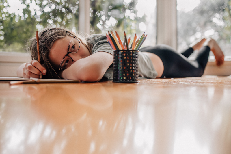young girl lying in front of a tin of coloured pencils