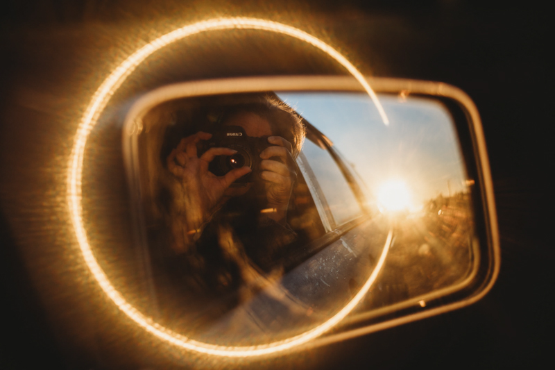 woman's reflection in car wing mirror surrounded by golden light