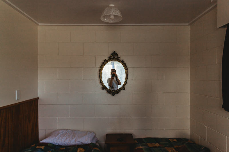 Interior of bedroom with woman's reflection in small wall mirror