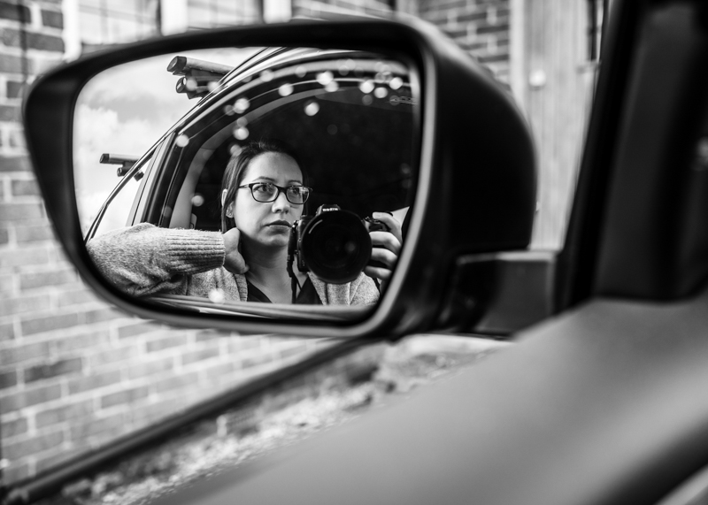 black and white portrait of woman reflected in car wing mirror