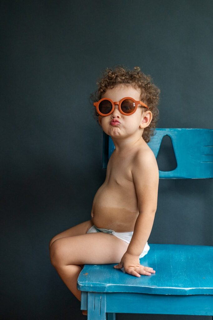 child on blue chair with sunglasses smiling with a cute face for the camera