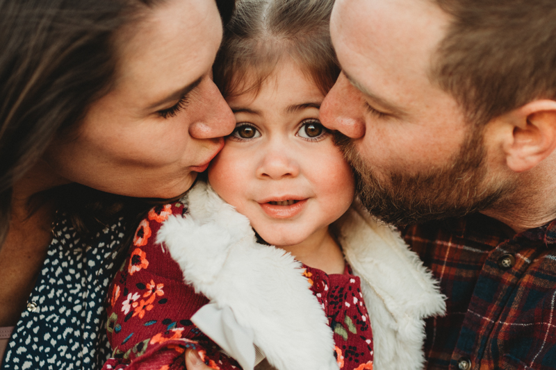family portrait of parents kissing toddler girl