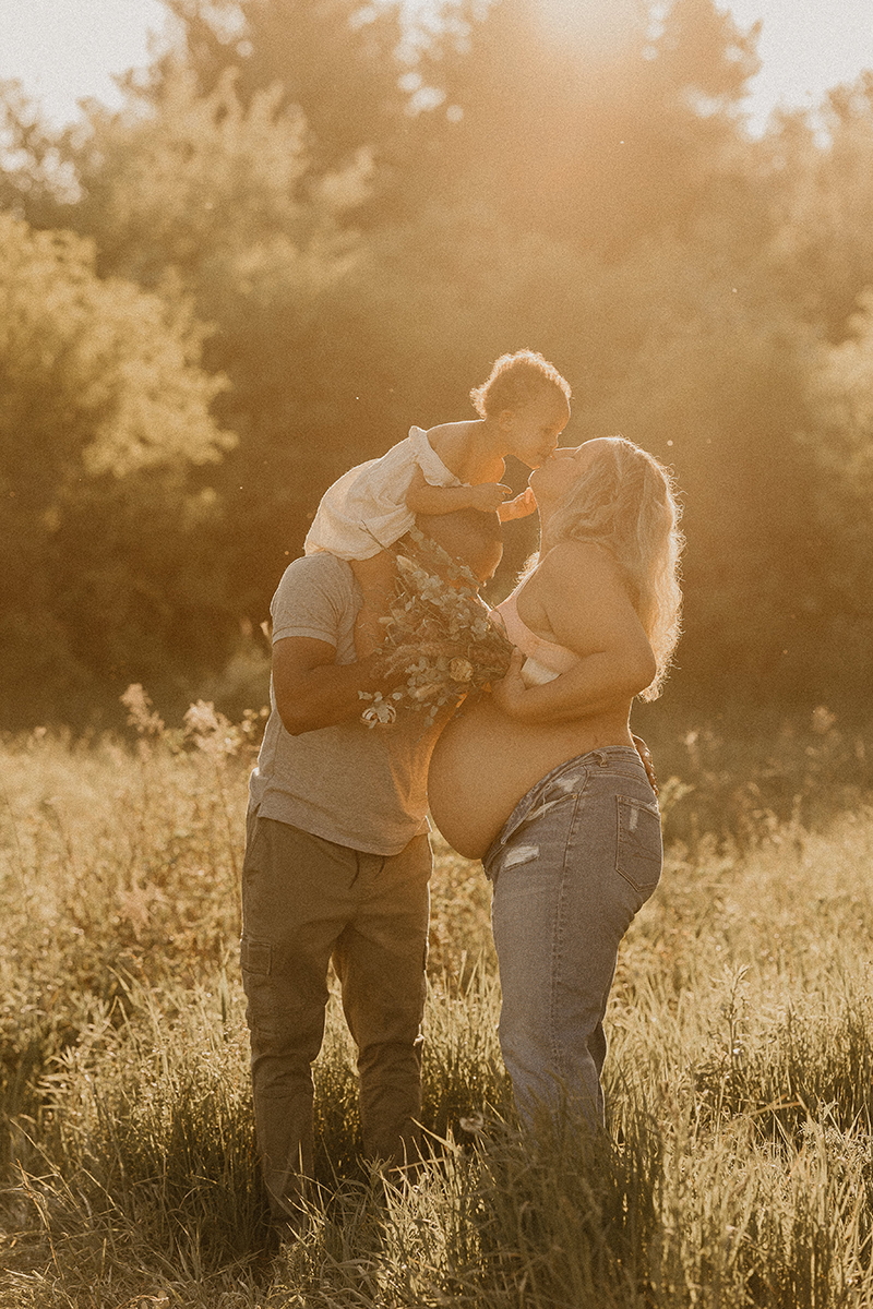 Pregnant mother, father and baby family photo with golden hour haze